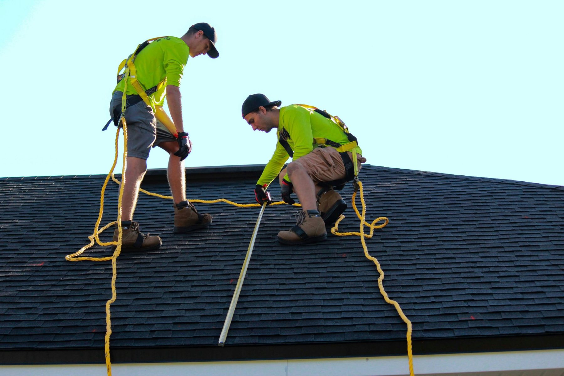 Two installers in safety harnesses measuring a roof before installation