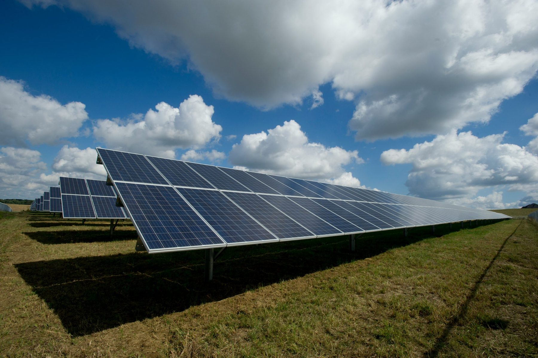 Ground-mounted solar array in an open field under a cloudy sky