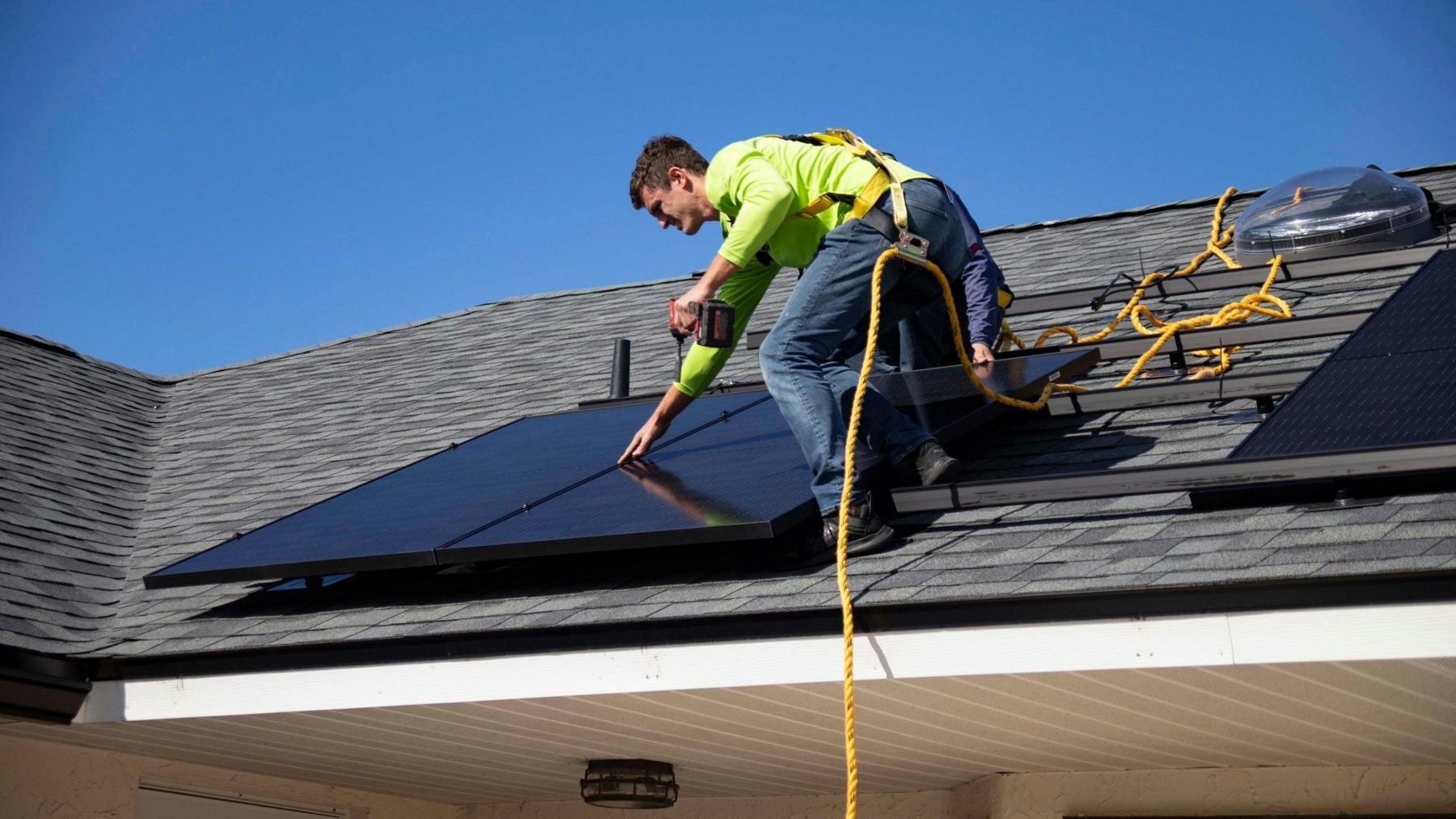 Installer in a safety harness securing solar panels on a shingle roof
