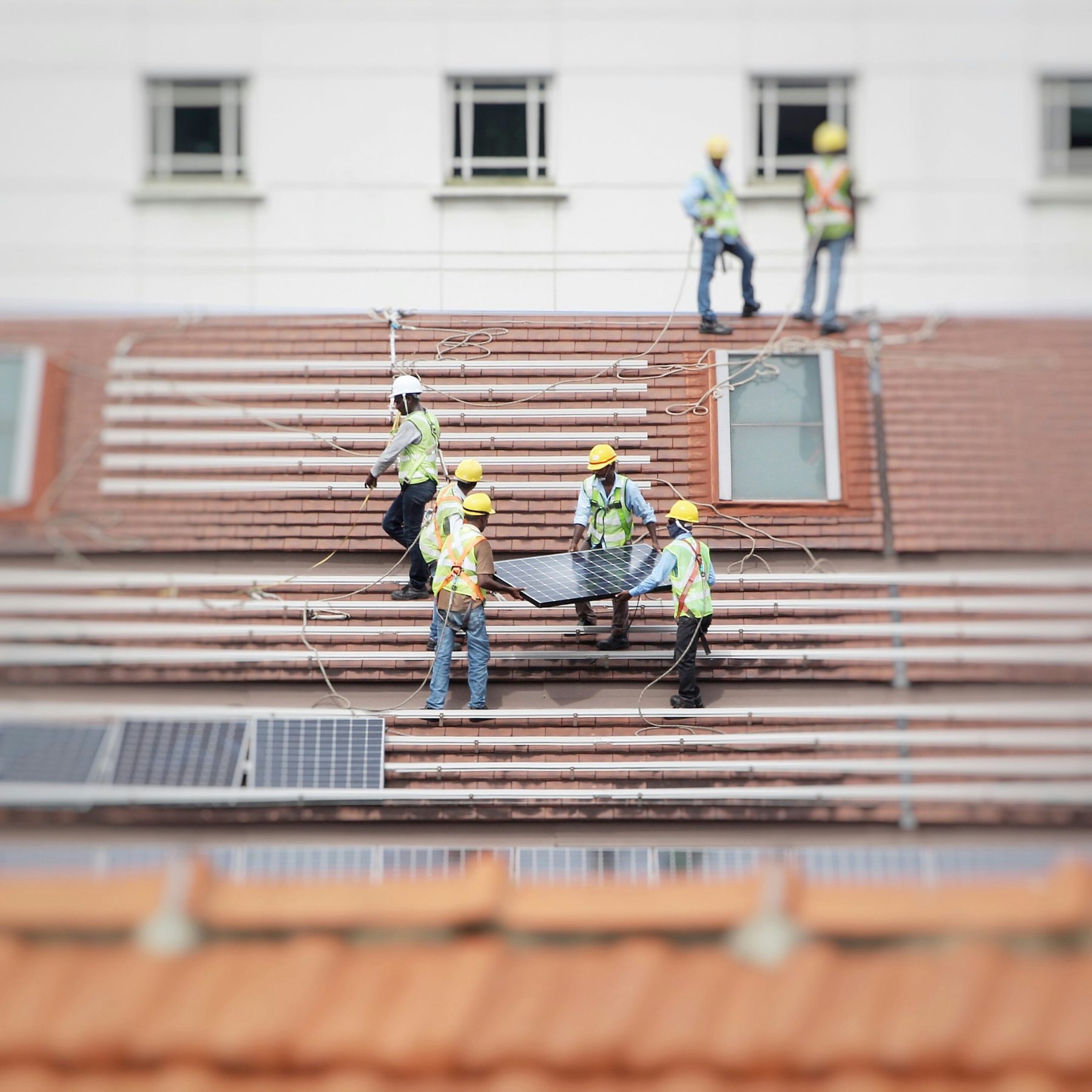 Installation crew in safety vests and hard hats carrying a solar panel across a tiled roof